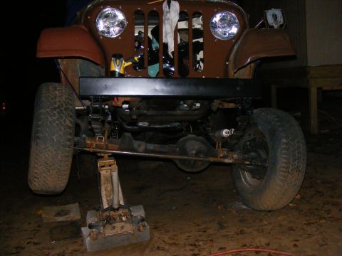 Front end of a brown Jeep CJ on a jack, showing suspension and grille