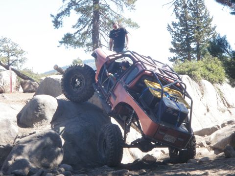 1961 International Scout 800 - Custom off-road vehicle with roll cage climbing over large rocks on a trail.