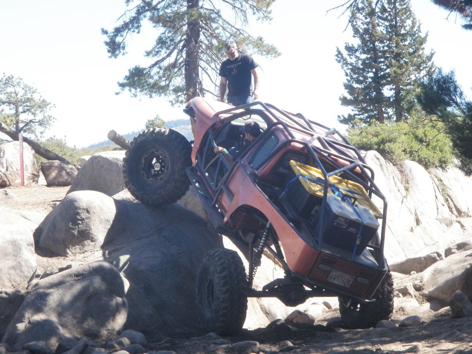 Custom off-road vehicle with roll cage climbing over large rocks on a trail