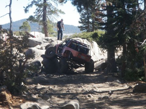 1961 International Scout 800 - A heavily modified off-road vehicle navigates a challenging rocky terrain on a sunny day.