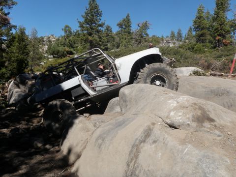 1961 International Scout 800 - Custom off-road vehicle with roll cage navigating large rocks on a sunny day.