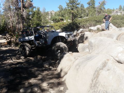 1961 International Scout 800 - A modified off-road vehicle navigates a challenging rocky trail under a clear blue sky.