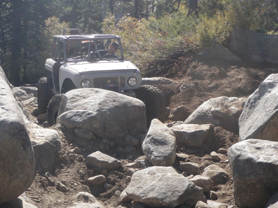 1961 International Scout 800 off-roading on a boulder-strewn trail, light-colored body, roll cage, driver visible
