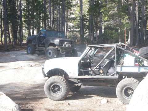 1961 International Scout 800 - Two modified off-road vehicles are parked on a dirt and rock path in a wooded area.