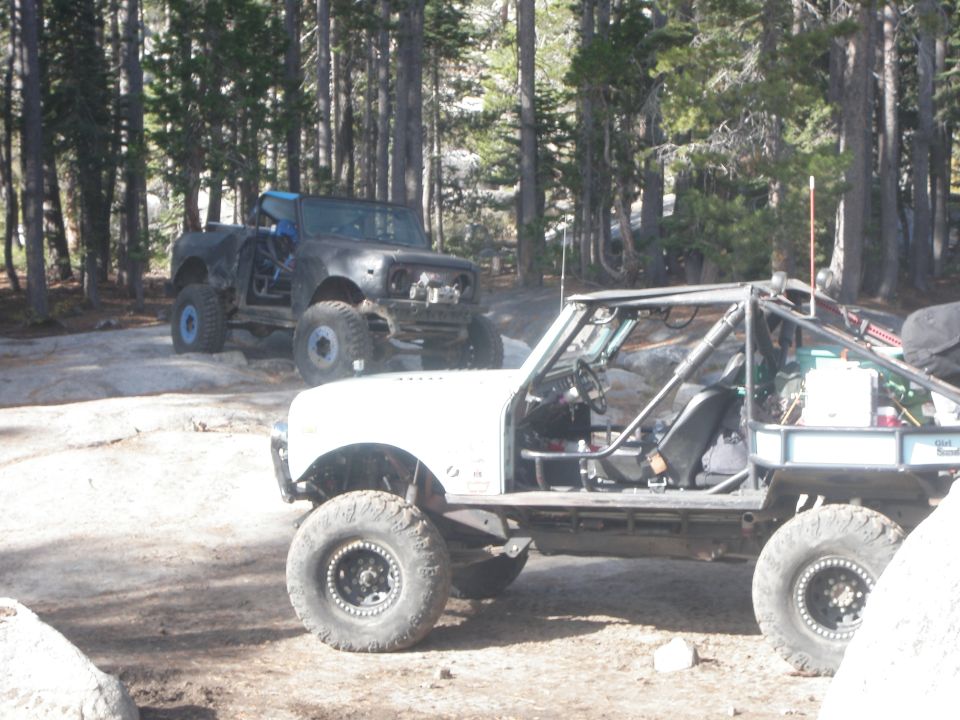 Two off-road vehicles parked in a forest clearing with trees and rocks