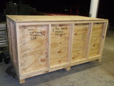 1970 Ford Mustang - A large wooden crate is shown in a workshop setting, with shipping information written on its sides.