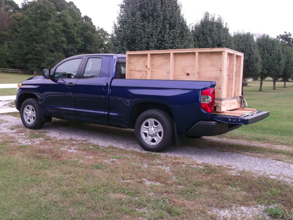 Blue pickup truck from rear, carrying a wooden crate