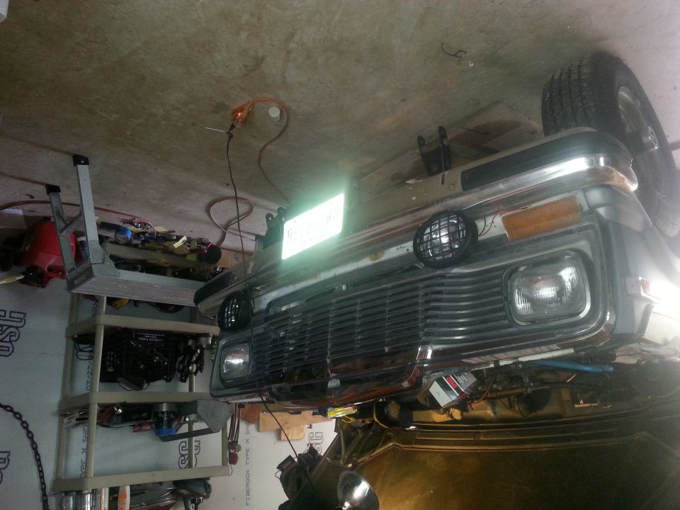 Front end of a pickup truck, possibly from the 70s or 80s, in a garage. It has a chrome grille and round headlights