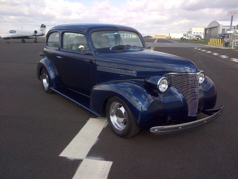 1939 Chevrolet Biscayne - A classic dark blue 1939 Chevrolet sedan sits on an airport tarmac with a private jet in the background.