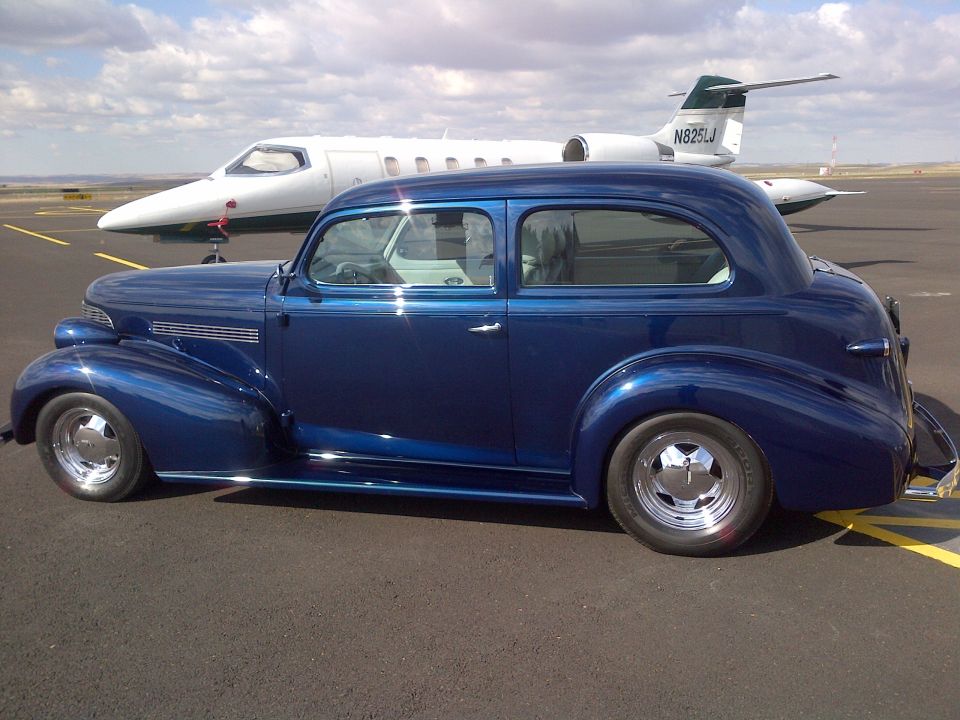 Blue sedan parked on tarmac next to a private jet. The jet has registration N825LJ