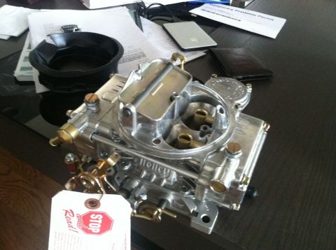 1978 Ford Bronco - A close-up of a shiny Holley carburetor sits on a dark surface next to various documents and a wallet.