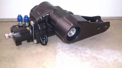 1996 Ford Bronco - A black steering gear box with blue hydraulic fittings and a metal mounting bracket is shown against a concrete floor.
