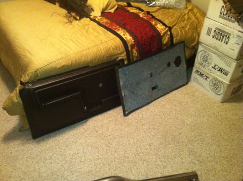 1982 Ford Bronco - A dark brown car door panel and its backing are laid out on a carpeted floor next to a bed.