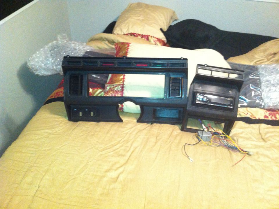 Dashboard pieces and car stereo with wires on a bed