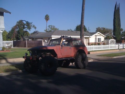 1968 Ford Mustang - A heavily modified off-road vehicle with large tires sits on a suburban street under a clear blue sky.