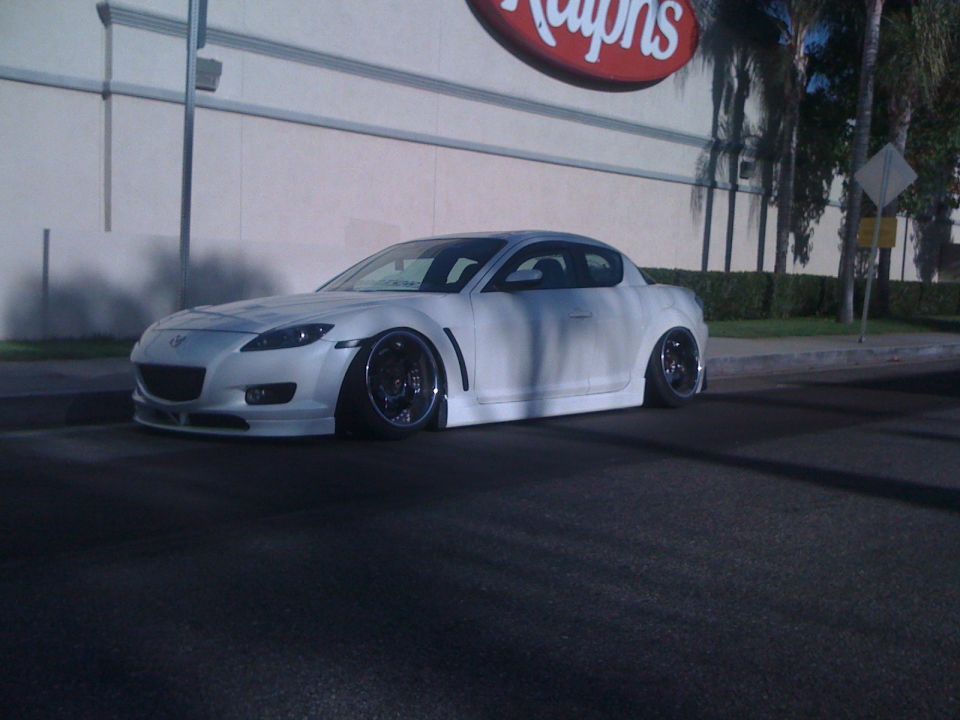 White sports car with lowered suspension parked in front of a building with a Ralphs sign