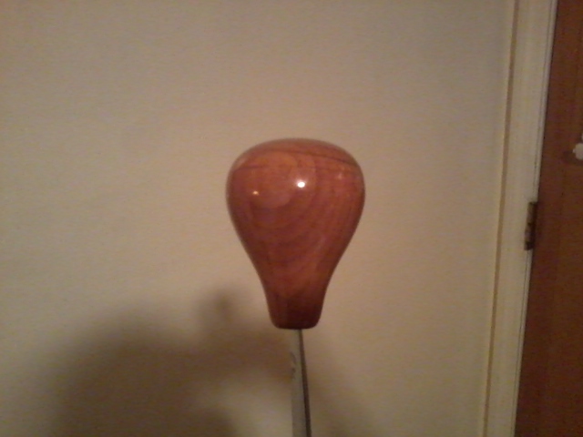 Wooden gear shift knob with visible grain, mounted on a metal shaft