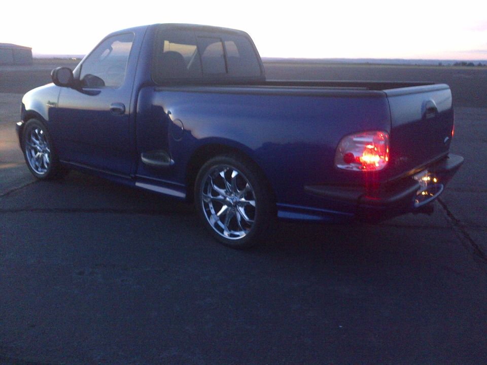 Blue pickup truck with custom rims parked on asphalt at dusk