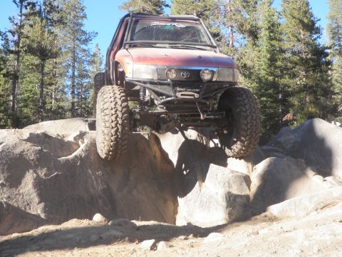 1961 International Scout 800 - Modified Toyota pickup truck navigates a rocky terrain with its front wheels elevated.