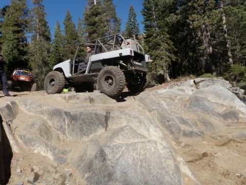 1961 International Scout 800 - An off-road vehicle with a prominent roll cage tackles a challenging rocky trail, with another vehicle visible in the background.
