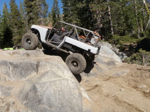 1961 International Scout 800 - Custom buggy with roll cage climbs over large rocks on a trail.