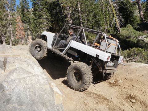 1961 International Scout 800 - Modified off-road vehicle navigates a rocky incline in a wooded area.