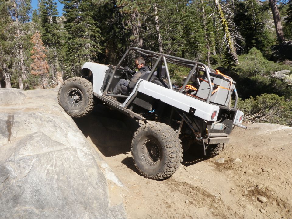 White off-road vehicle with roll cage climbing a rock, driver visible