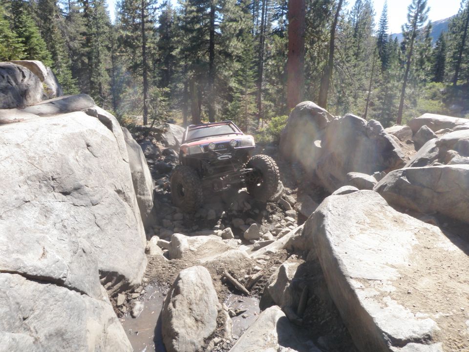Modified off-road vehicle with large tires climbing over rocks and mud