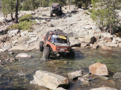 1961 International Scout 800 - Two off-road vehicles navigate a rocky stream bed on a sunny day.