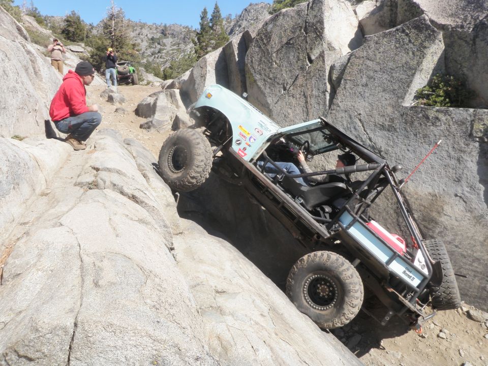 Off-road vehicle navigating a steep, rocky incline with people watching