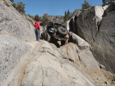 1961 International Scout 800 - A modified off-road vehicle tackles a challenging rocky trail with onlookers present observers watching.