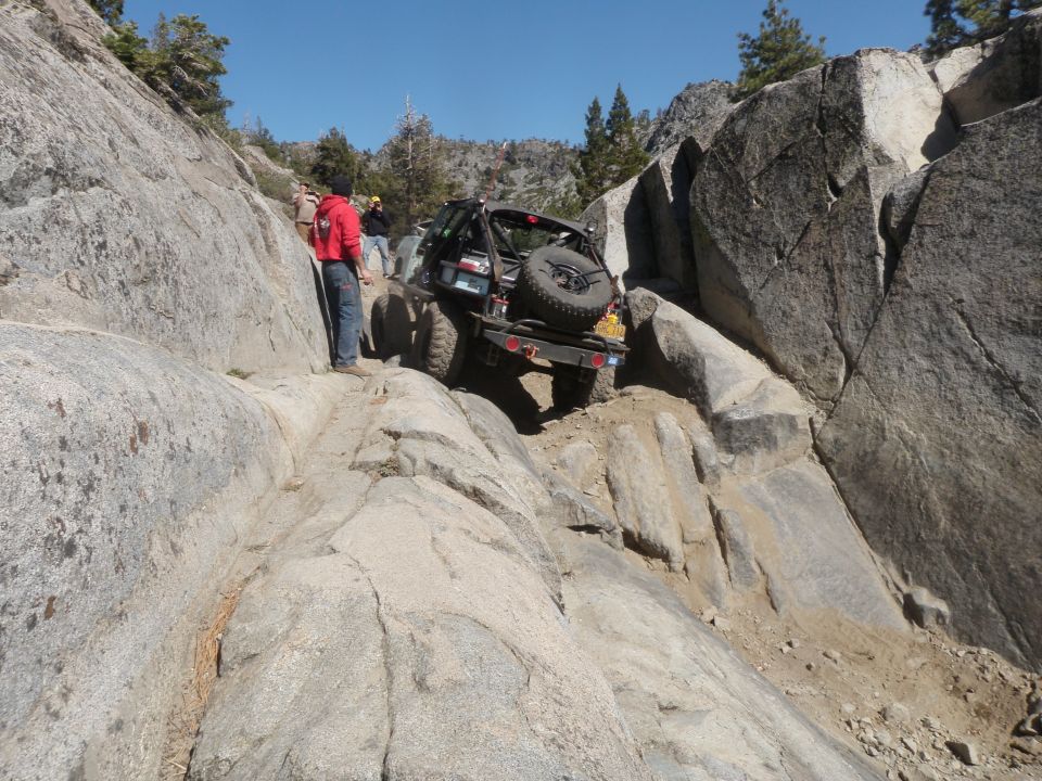 Black off-road vehicle with spare tire on rear, navigating a rocky incline