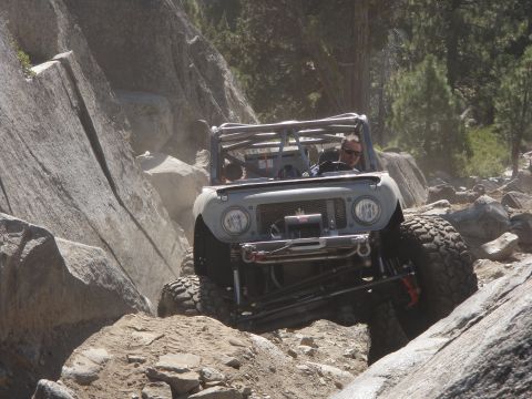 1961 International Scout 800 - A 1961 International Scout 800 navigates a challenging rocky terrain with a roll cage and large off-road tires.