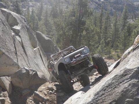 1961 International Scout 800 - A heavily modified 1961 International Scout 800 navigates a steep, rocky trail in a mountainous, forested area.