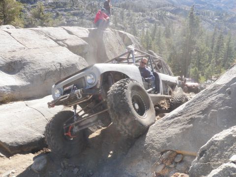 1961 International Scout 800 - A heavily modified off-road vehicle navigates a challenging rocky terrain with spectators observing the action.