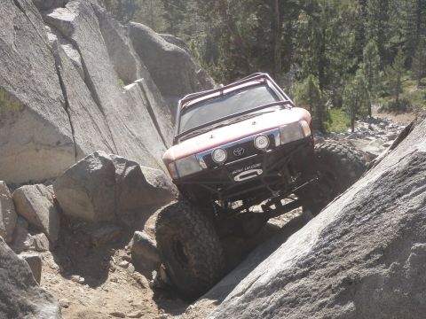 1961 International Scout 800 - A modified red Toyota 4Runner navigates a challenging rocky terrain with its large off-road tires and winch visible.