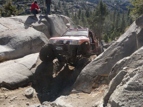1961 International Scout 800 - An off-road vehicle navigates a challenging rocky terrain, with two people observing from a boulder above.