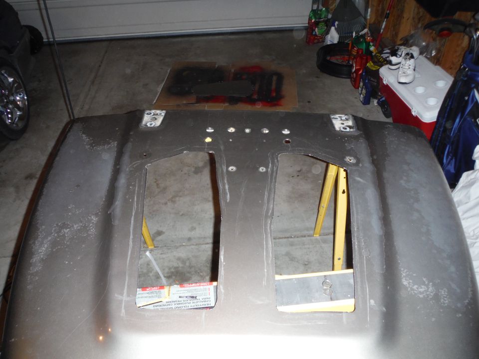 vehicle hood with two large cutouts, resting on sawhorses in a garage