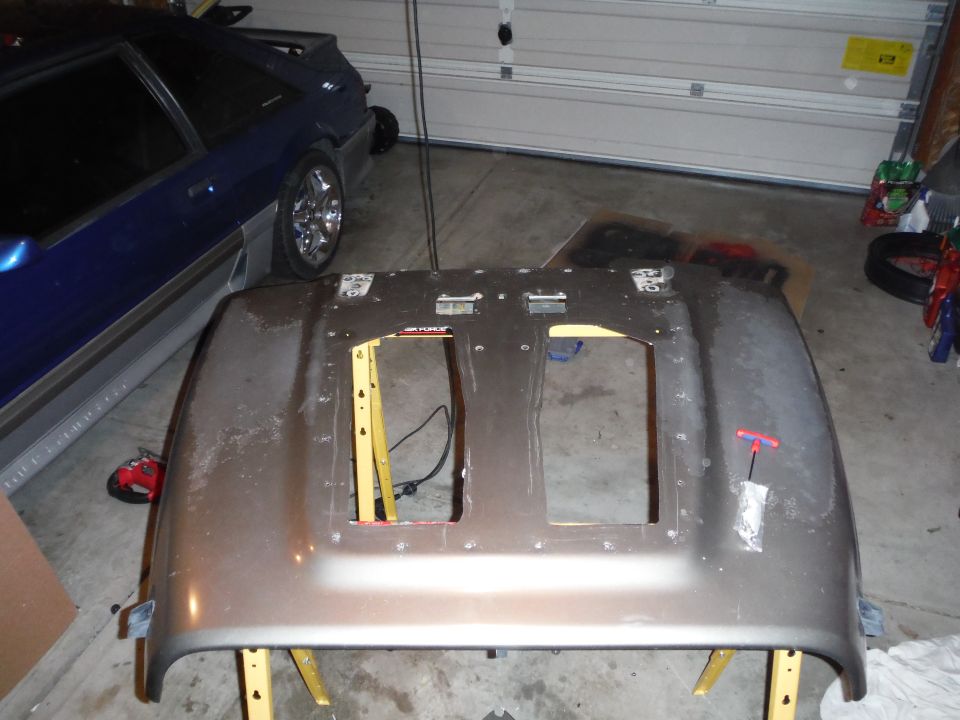 Car hood on sawhorses in a garage, with a blue car in the background