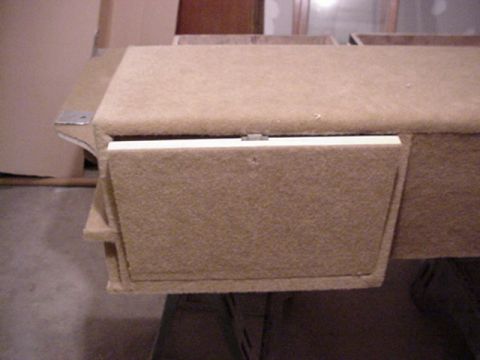 1993 Ford Bronco - End detail of a carpet-wrapped custom console showing one hinged access door and a small side-loading drawer partly pulled out, with a pian…