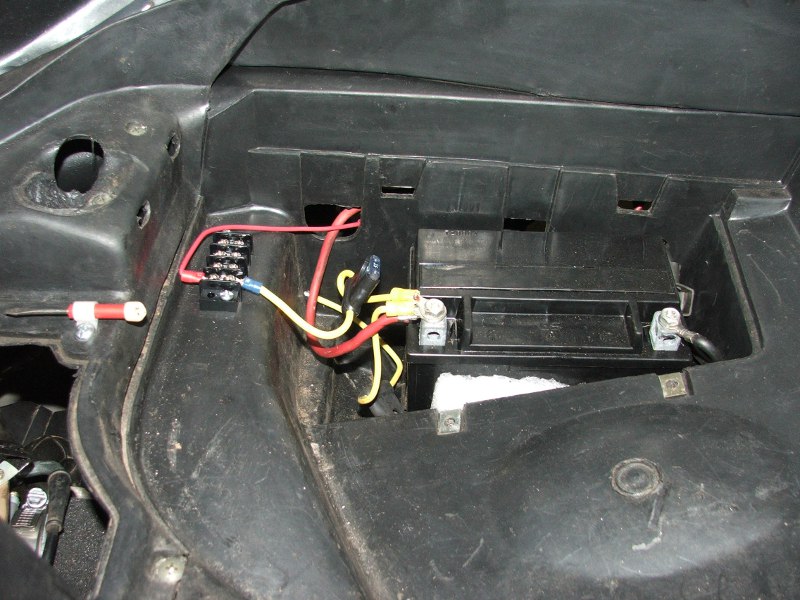 Motorcycle battery with red and yellow wires connected to a fuse block and terminal