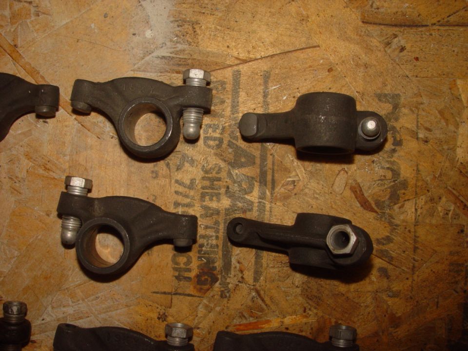 Several engine rocker arms are laid out on a wooden surface. Some have bolts attached