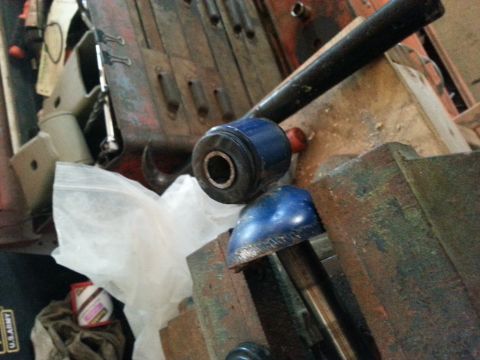 1982 Jeep Wagoneer - Automotive parts, including a blue bushing and a metal component, are secured in a vise within a workshop setting.