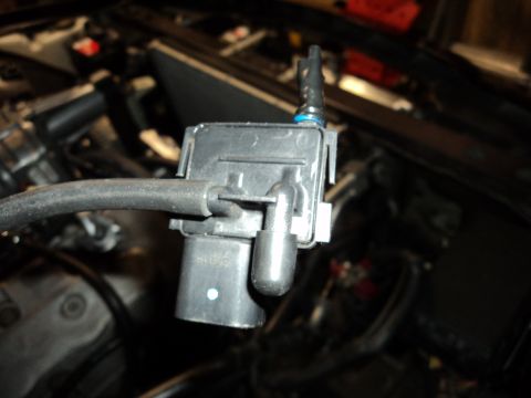 2004 Mercury Grand Marquis - A close-up view of a black plastic engine component with attached hoses. Some text is visible on the part.
