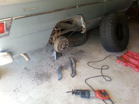 1982 Jeep Wagoneer - A gray Jeep Wagoneer is undergoing repairs, with its rear wheel off and tools laid out on the concrete floor.