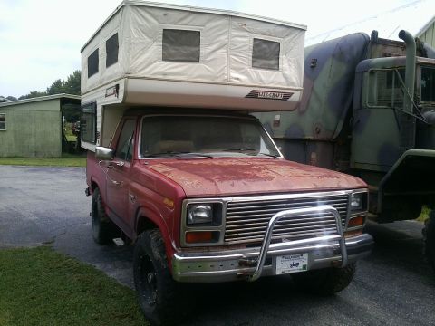 1984 Ford Bronco - This red pickup truck is equipped with a Lite-Craft camper shell and a front brush guard. Another vehicle is parked to its right.
