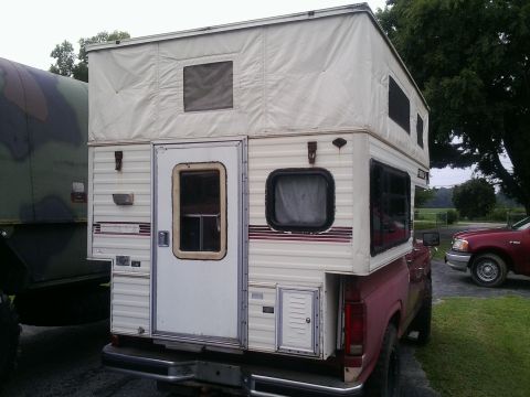 1984 Ford Bronco - A pickup truck is fitted with a pop-up camper, parked next to another vehicle.