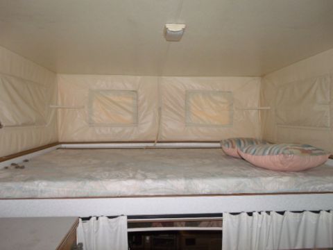 1984 Ford Bronco - The interior of a camper features a sleeping area with a mattress and pillows, and windows with fabric coverings.