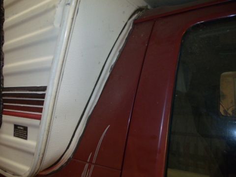 1984 Ford Bronco - Close-up of a red vehicle's side panel and a white camper shell, showing a partial view of both.