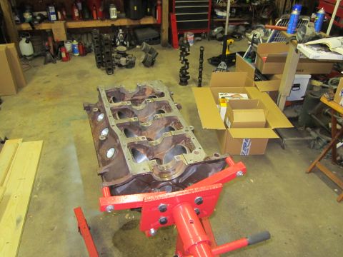 1984 Ford Bronco - Engine block on a stand in a garage setting, surrounded by various automotive parts and storage.